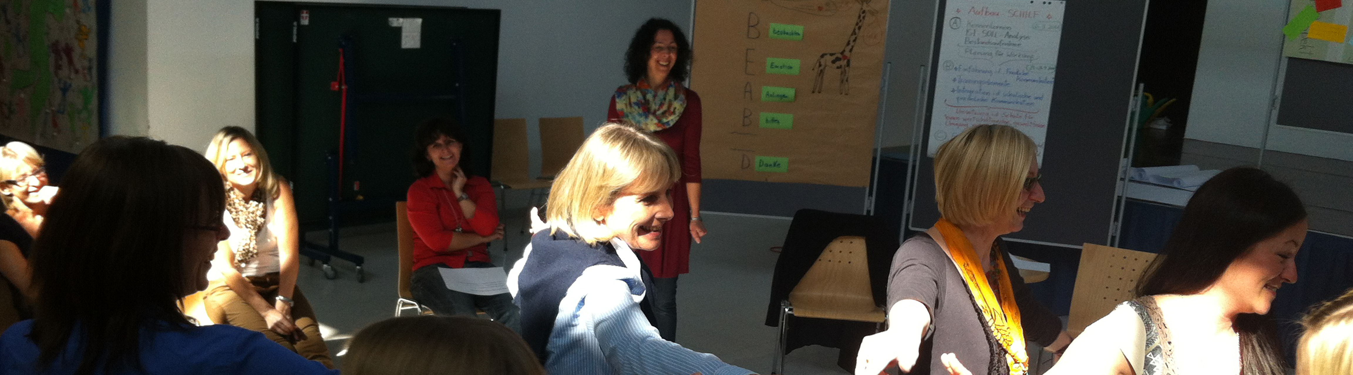 Fortbildungsteilnehmerinnen sitzen im Kreis und lächeln im Seminar "Selbstbehauptung durch Friedliche Kommunikation", ZIMD