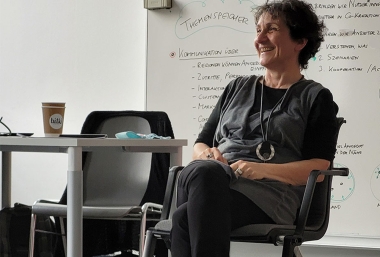 Dorothea Erharter sitzt vor einem Whiteboard auf dem "Themenspeicher" steht und lächelt, Workshop Gender Didaktik in MINT-Fächern, ZIMD