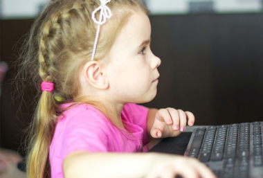 Kleines Mädchen sitzt vor dem Computerbildschirm und bedient die Maus. ZIMD