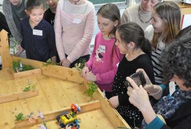 Eine Gruppe Mädchen steht am Werktisch und betrachtet die selbst gebauten Roboter, Workshop Roberta, ZIMD