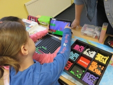 Zwei Mädchen sitzen an einem Tisch und arbeiten mit dem Tablet und ihrem "Bloxels"-Bausatz aus bunten Steinen. "Bloxels", ZIMD