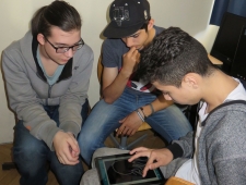 Drei jugendliche Burschen sitzen im Kreis. Ein Bursch zeichnet eine Grafik mit dem Finger auf dem Tablet, "Pocketcode", ZIMD