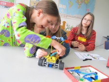Drei Mädchen bauen an ihrem bunten Roboter. Ein Mädchen steckt ein Bauteil an. "Roberta", ZIMD