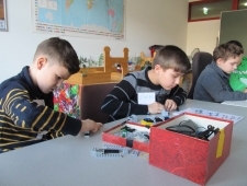 Vier Buben sitzen an einem Tisch und bauen ihren persönlichen Roboter aus Lego zusammen. Vor ihnen steht eine Schachtel mit Bauteilen und Kabeln. "Roberta", ZIMD