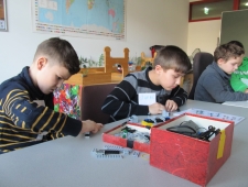 Roberta, ZIMD Vier Buben sitzen an einem Tisch und bauen ihren persönlichen Roboter aus Lego zusammen. Vor ihnen steht eine Schachtel mit Bauteilen und Kabeln. "Roberta", ZIMD
