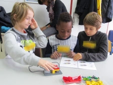 Drei Buben sitzen an einem Tisch. Zwei von ihnen lesen die Bauanleitung für ihren Roboter. Der Bub links baut am Roboter. "Robina", ZIMD